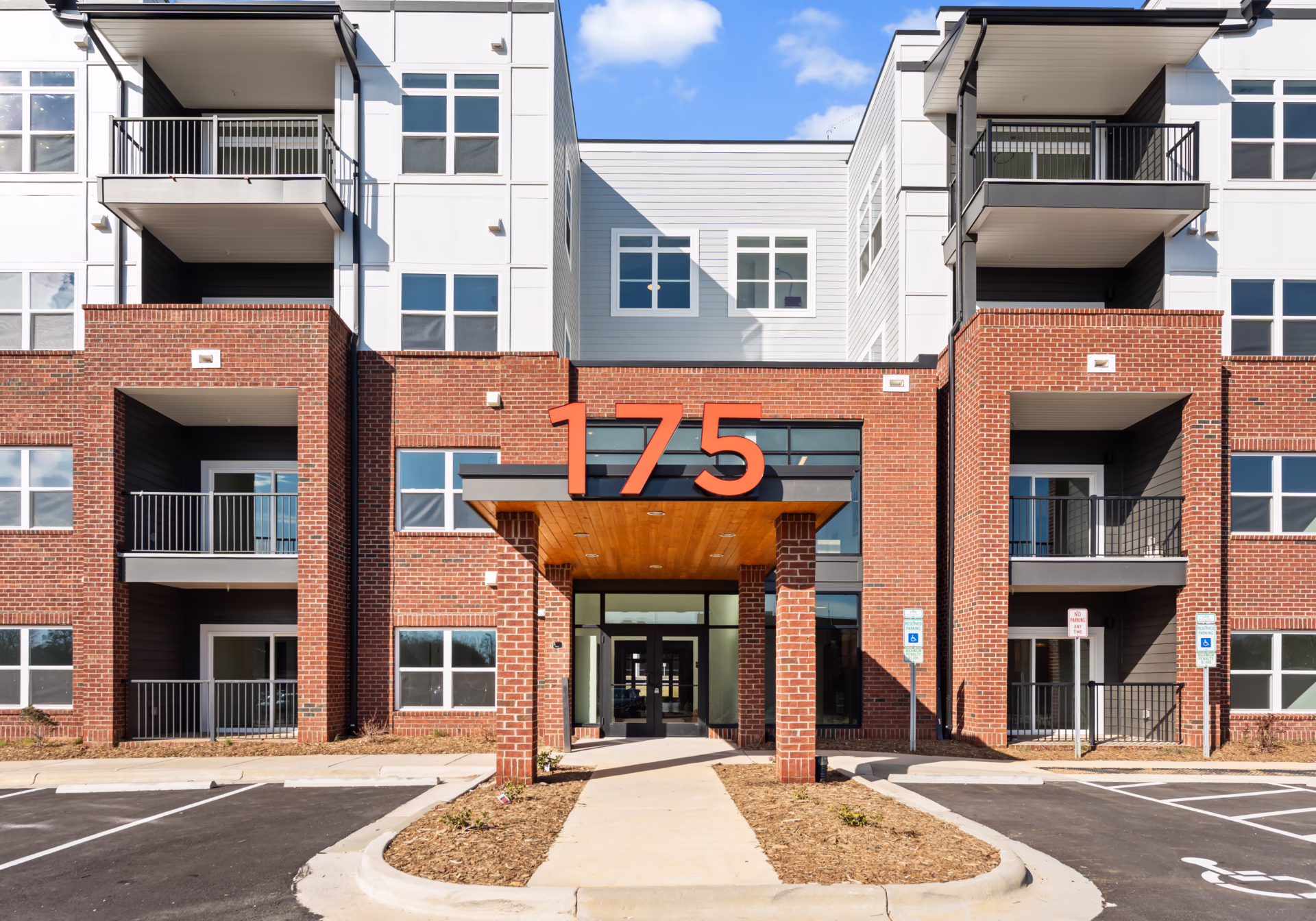 The corner entrance of Brixton Apartments: red 175 numerals mounted on a corten steel canopy above the glass doors, framed by red brick piers.
