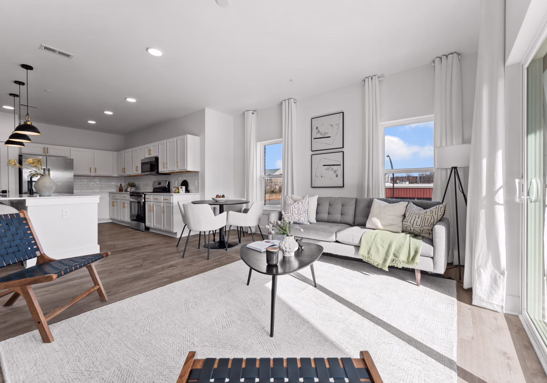 A two-bedroom living area open to the kitchen, with tall windows and a sliding balcony door.
